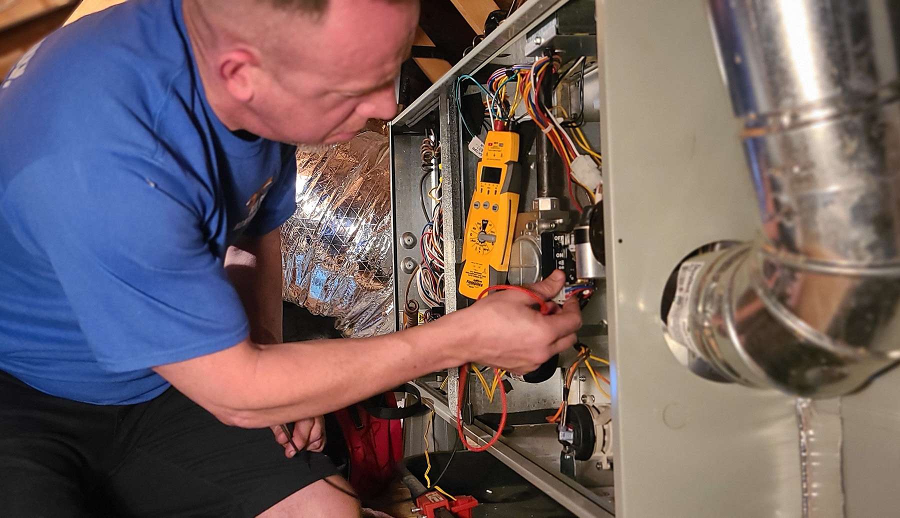 Fox Family Heating & Air Conditioning technician using diagnostic tools to test electrical components inside a furnace.