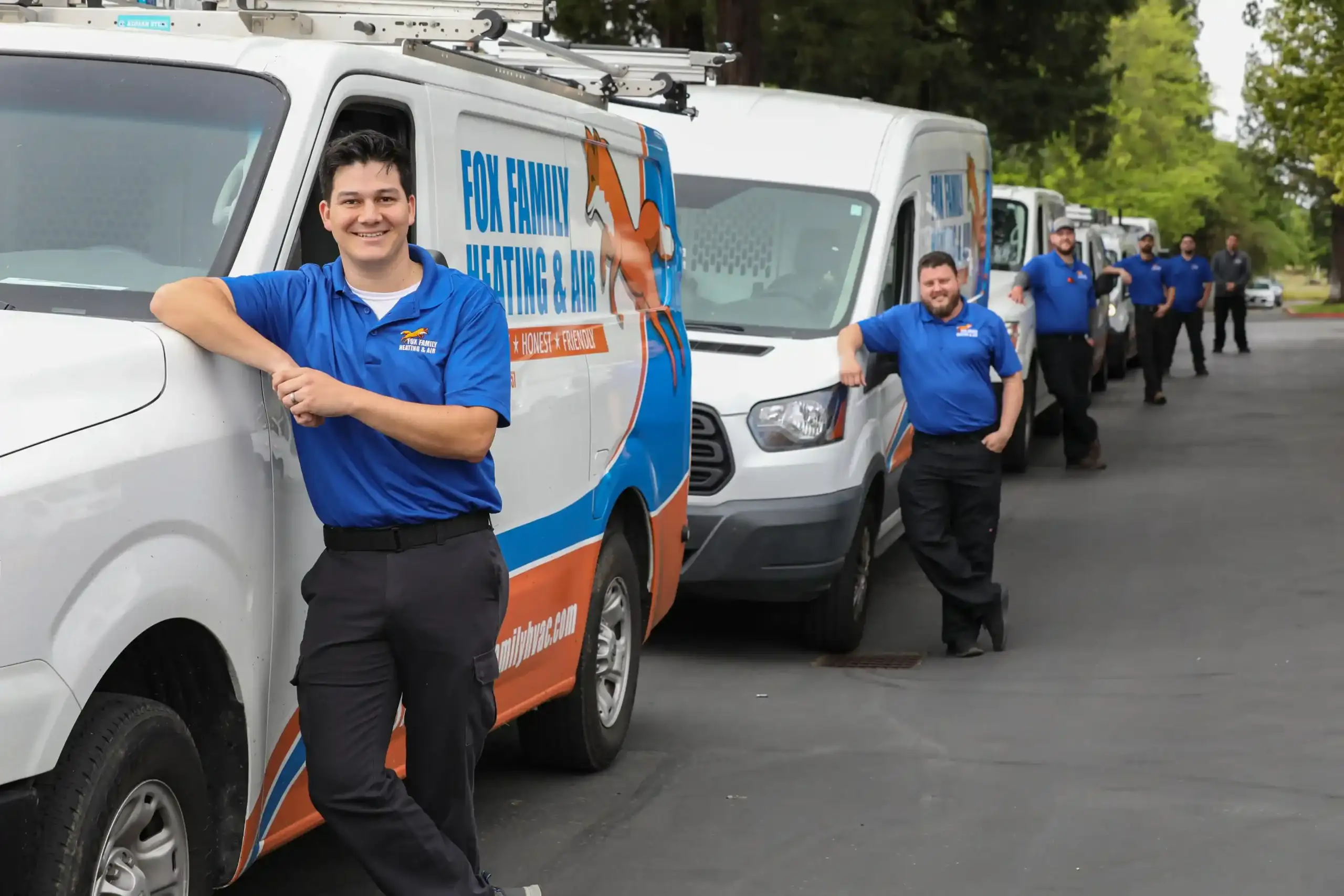 Fox Family Heating & Air Conditioning technicians standing beside branded service vans in a lineup.