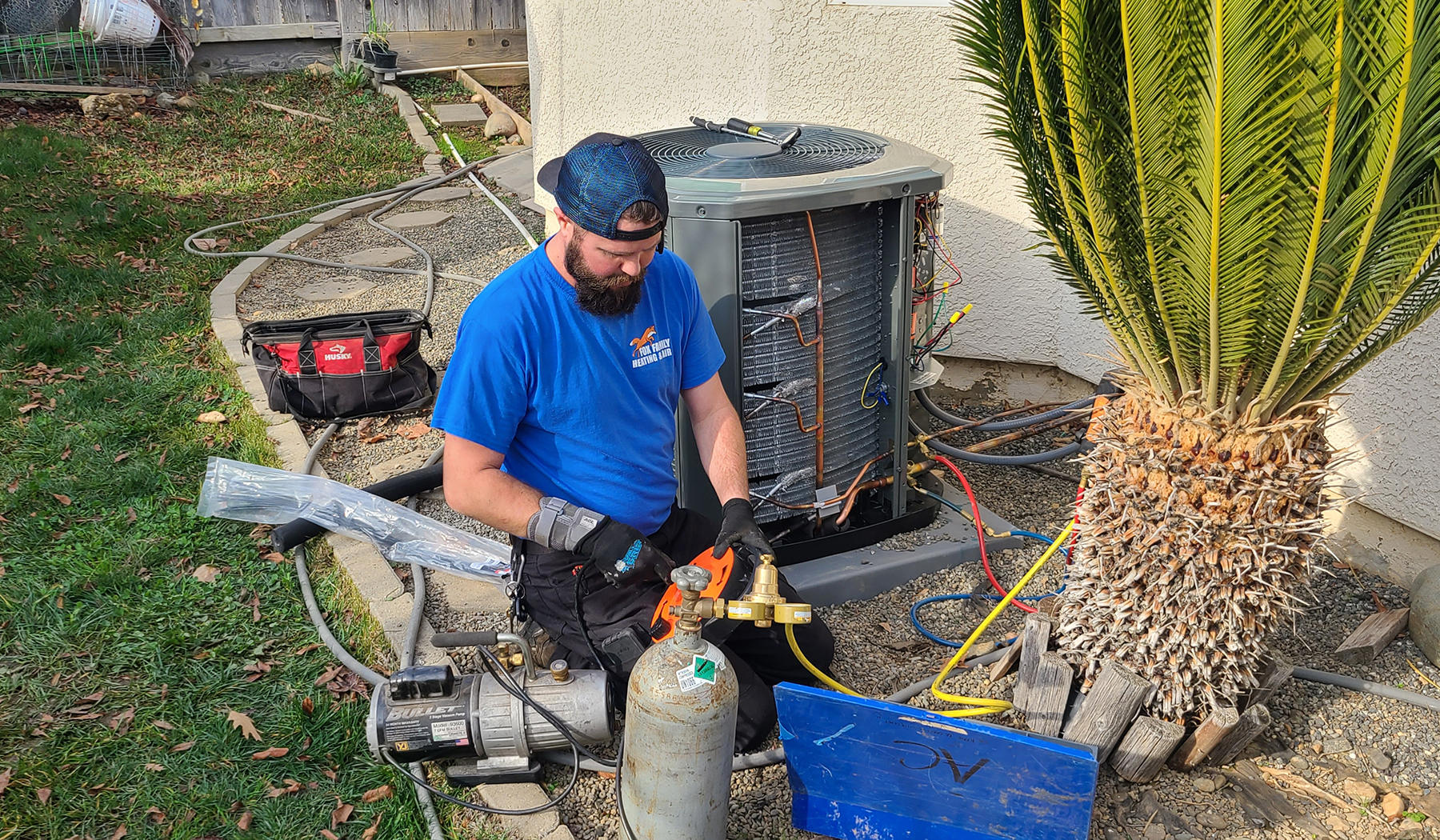 Fox Family Heating & Air Conditioning technician working on an outdoor AC installation, connecting refrigerant lines and equipment.