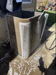 Technician rinsing buildup from an outdoor AC condenser coil during maintenance in Sacramento