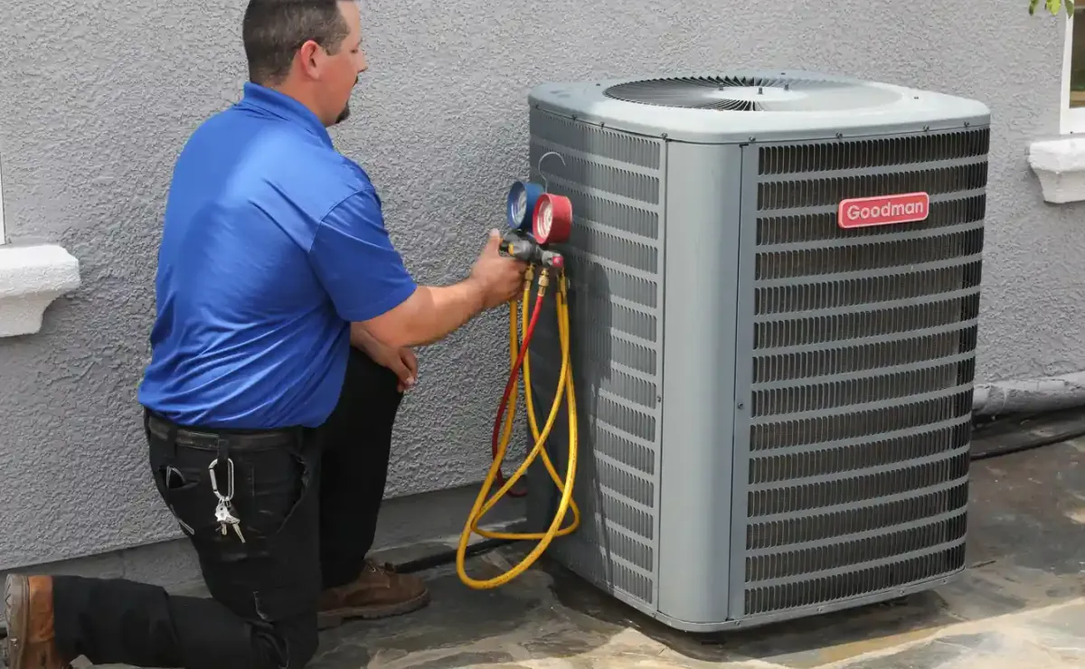 HVAC technician kneeling beside Goodman outdoor air conditioner unit performing pressure testing with manifold gauges