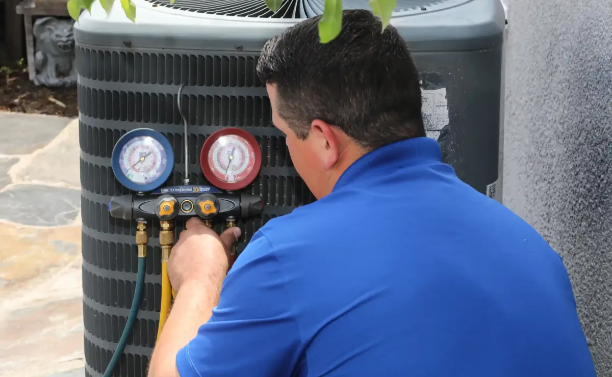 HVAC technician in blue Fox Family uniform using red and blue pressure gauges to test outdoor AC condenser unit